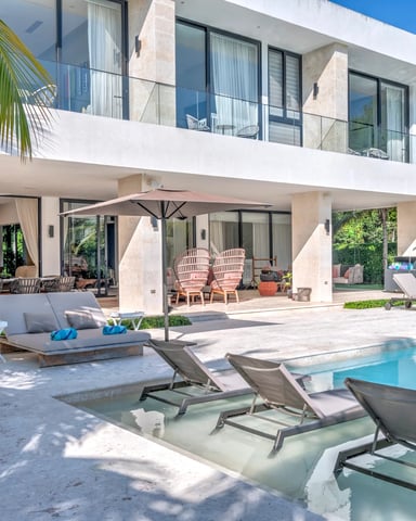 Modern white villa with pool, lounge chairs, covered patio, and palm trees surrounding the property