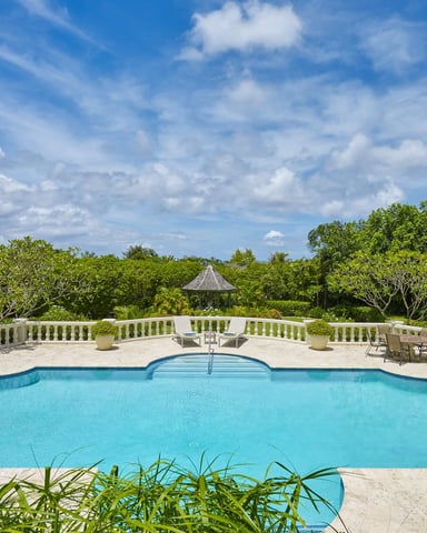 Resort swimming pool with stone deck, balustrade, and tropical vegetation under blue sky