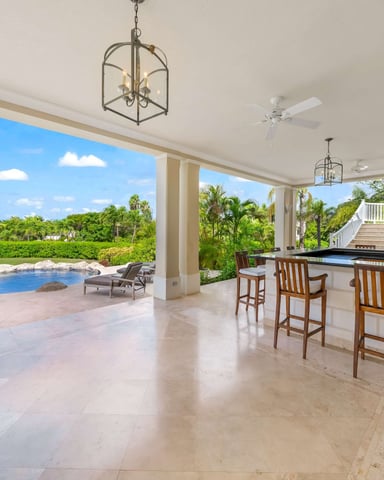 Covered patio with outdoor kitchen, bar seating, and pool overlooking tropical landscape