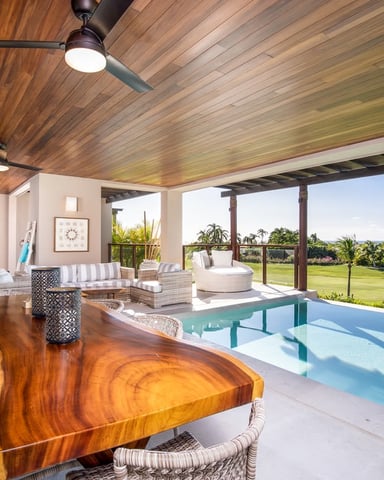 Covered patio with wood ceiling, dining table, lounge seating, and infinity pool overlooking golf course and palm trees