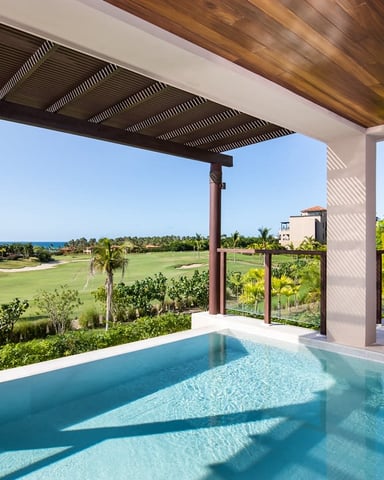 Infinity pool on covered terrace overlooking golf course, ocean, and tropical landscaping