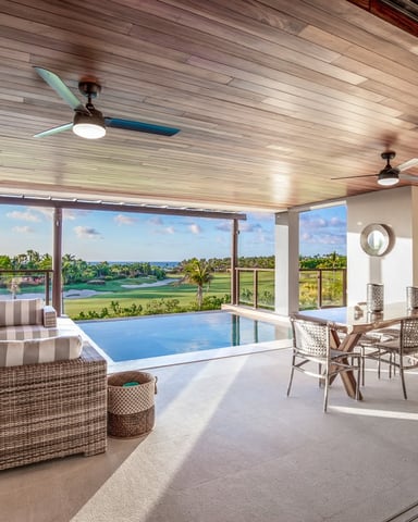 Luxury indoor pool room with wicker seating, ceiling fans, and expansive windows overlooking golf course and water views