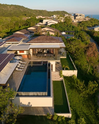 Modern hilltop villa with swimming pool, terrace, and sea view, surrounded by Mediterranean vegetation and neighboring stone houses