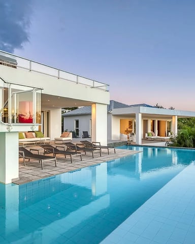 Modern white villa with infinity pool, lounge chairs, and tropical landscaping at dusk