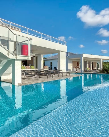 Modern white villa with infinity pool, lounge chairs, and tropical landscape under blue sky
