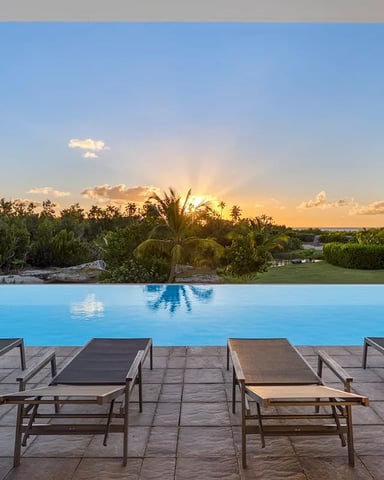 Infinity pool with lounge chairs overlooking tropical landscape at sunset, modern white house on right
