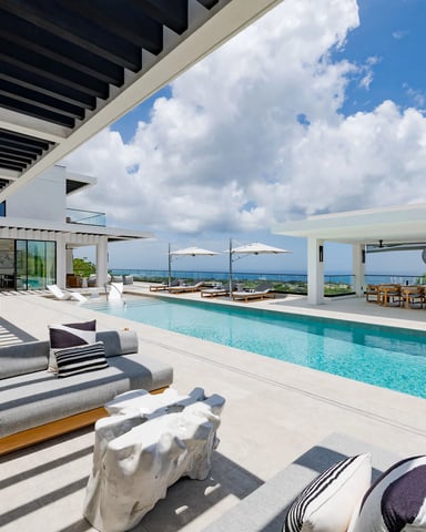 Modern oceanfront villa with infinity pool, lounge chairs, pergola, and panoramic sea views under blue sky