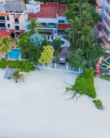 Aerial view of beachfront resort with white sand, colorful umbrellas, pools, and multi-story buildings with red roofs