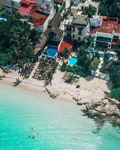 Aerial view of beachfront resort with colorful buildings, pools, palm trees, and turquoise water