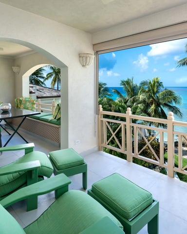 Beachfront terrace with green lounge chairs, dining area, and turquoise ocean view beyond wooden railing