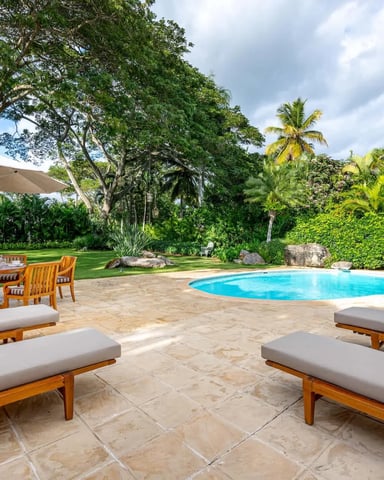 Tropical backyard with swimming pool, wooden lounge chairs, dining table with umbrella, palm trees, and manicured lawn