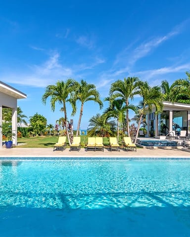 Resort-style pool with turquoise water, lounge chairs, palm trees, and modern white pavilions overlooking ocean view