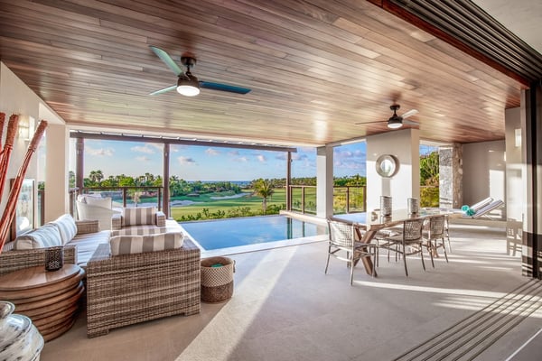 Luxury indoor pool room with wicker seating, ceiling fans, and expansive windows overlooking golf course and water features