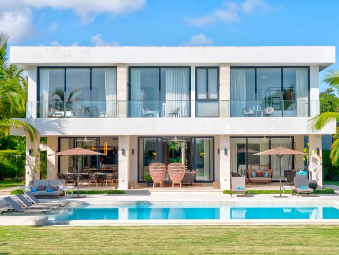 Modern two-story white house with swimming pool, lounge chairs, and palm trees surrounding the property